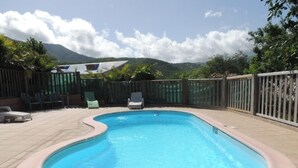A swimming pool with a curved edge, surrounded by a wooden fence and chairs.