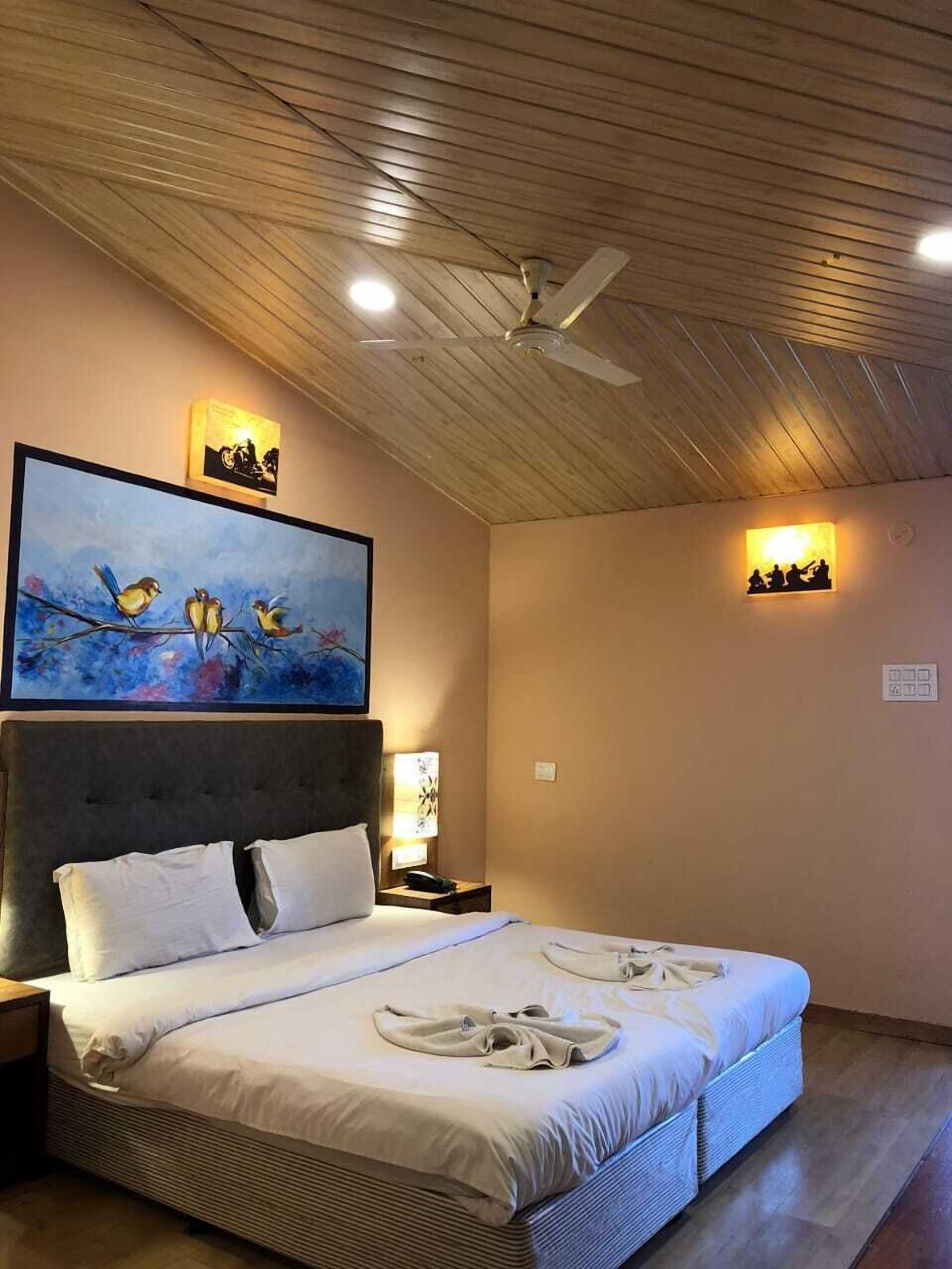 Une chambre avec un grand lit, un ventilateur de plafond et des œuvres d’art accrochées aux murs.