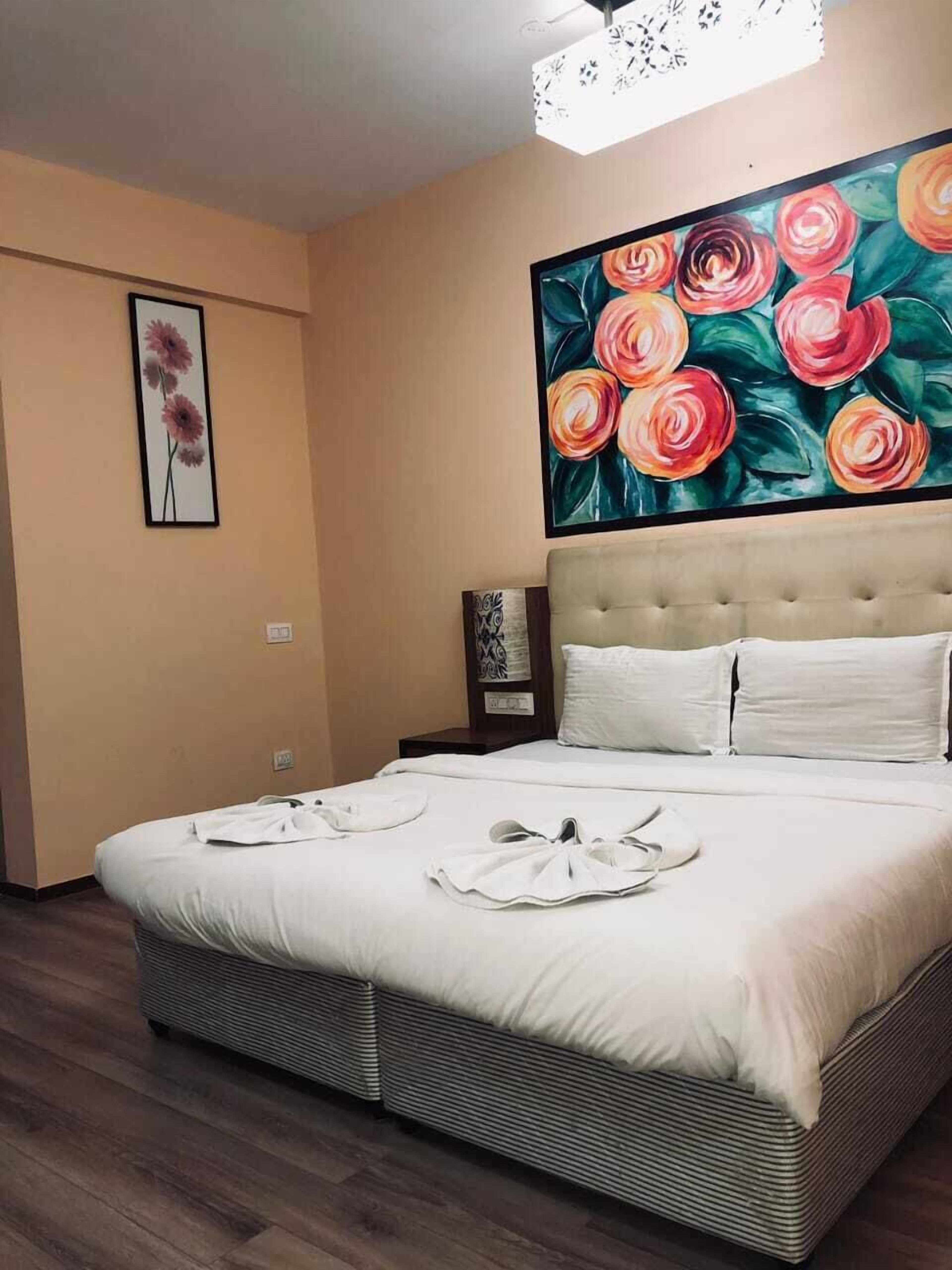 A neatly made bed with white linens and a large painting of flowers above it.
