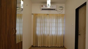Un couloir avec une porte en bois, un rideau beige et un appareil de climatisation fixé au mur.