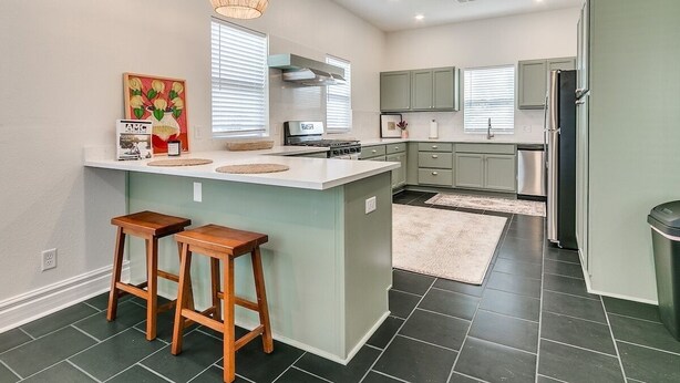 Een moderne keuken met een centraal eiland, barkrukken, een hanglamp en een geïntegreerde kookplaat.