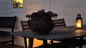 Una terraza de madera con una mesa, sillas, una planta en maceta y un farol.
