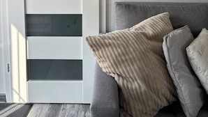 Una habitación con puerta corredera, un sofá gris con cojines y una pared de madera.