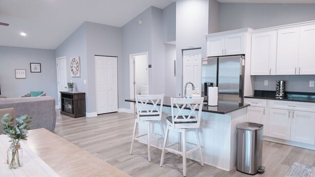 Una cocina moderna con armarios blancos, un refrigerador de acero inoxidable y un comedor con dos sillas blancas.