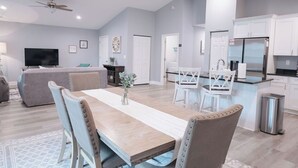 Una sala de estar moderna con una mesa de comedor de madera, sillas tapizadas en azul claro, un sofá gris y un televisor de pantalla plana.