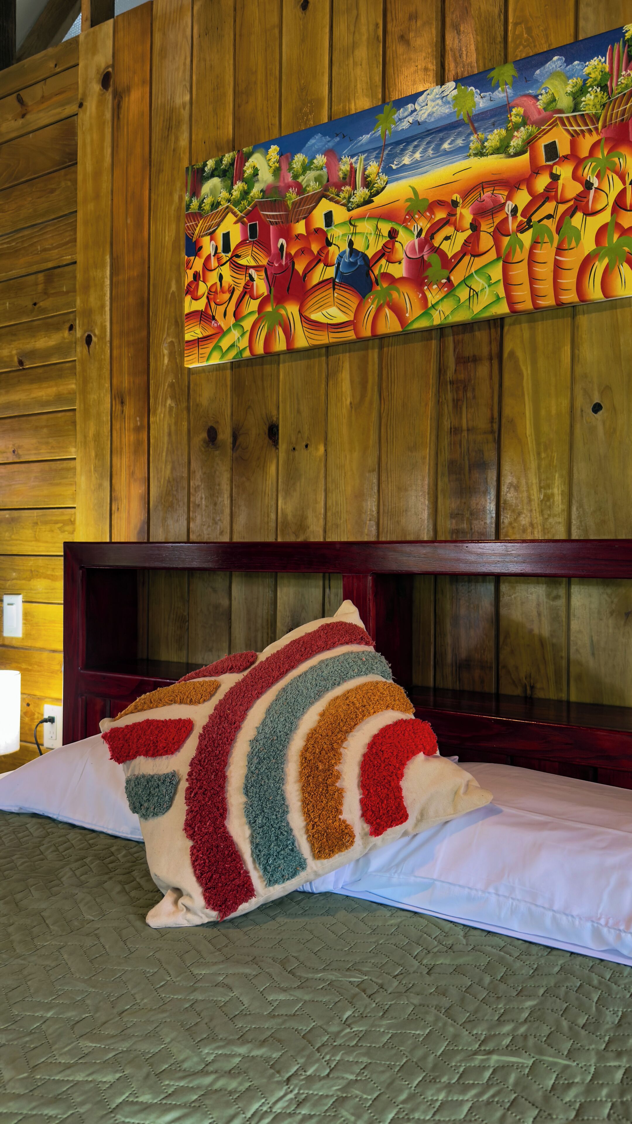 A bed with a colorful pillow and a painting above it.