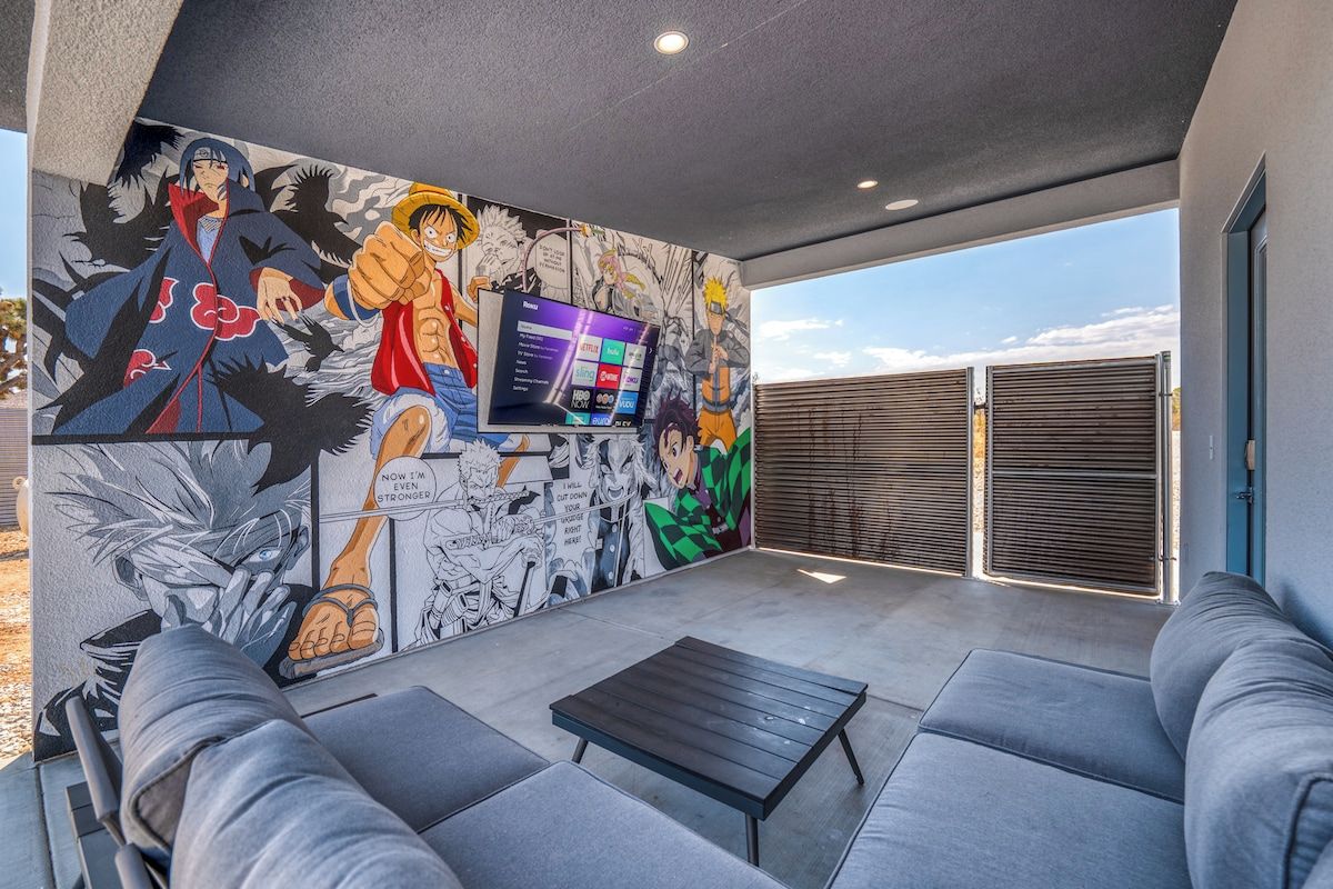 A modern outdoor seating area with a mural, a flat-screen TV, and a view of the sky.