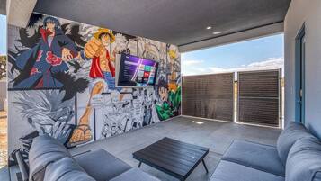 A modern outdoor seating area with a mural, a flat-screen TV, and a view of the sky.