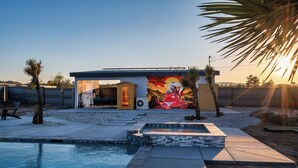 A modern outdoor pool area with a mural, a small building, and a clear sky. - Saltwater Pool/Sauna/Mini Golf/JT Nat Park/Firepit (Yucca Valley)
