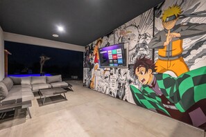 Een moderne woonkamer met een grote televisie, een bank en een wanddecoratie met anime personages.