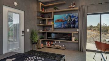 Een moderne woonkamer met een grote flatscreen televisie, inbouwkasten, een gezellige zithoek en uitzicht door een schuifdeur.