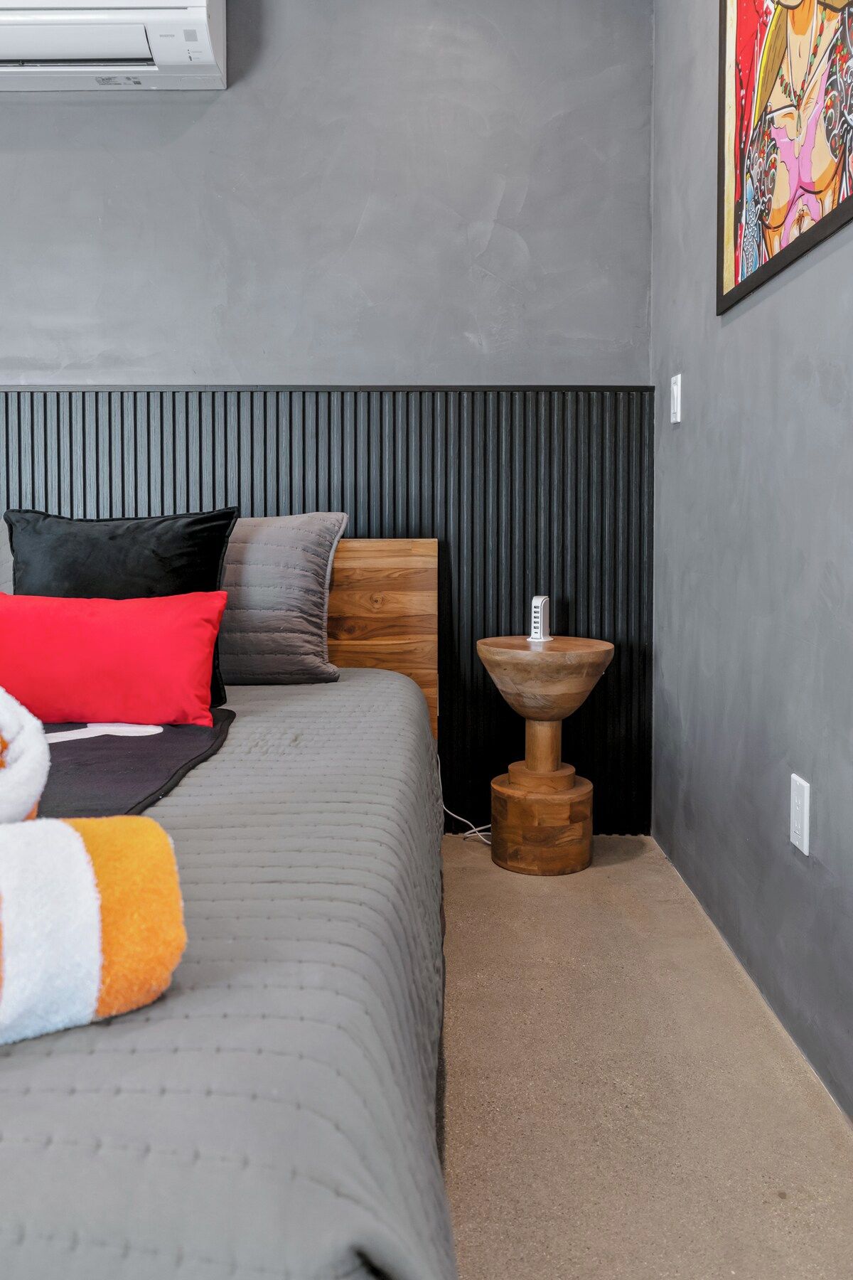 Une chambre à coucher avec un lit, des oreillers, une table de chevet et un climatiseur fixé au mur.