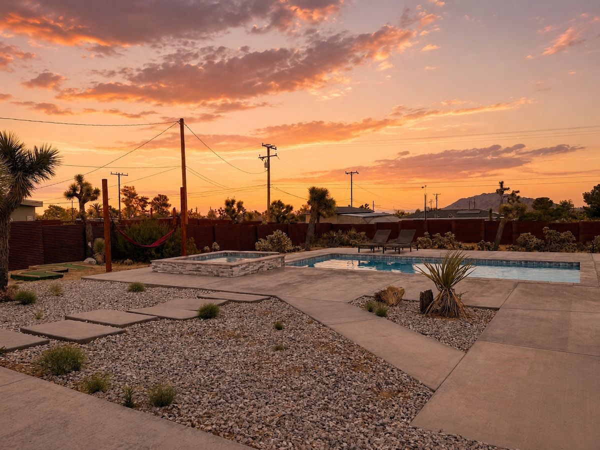 Un espace piscine offrant une vue sur le coucher de soleil, entouré d’un jardin aménagé avec des rochers et des plantes.