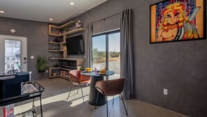 A modern living room with a large TV, a dining table with chairs, and a large window with curtains. - Saltwater Pool/Sauna/Mini Golf/JT Nat Park/Firepit (Yucca Valley)