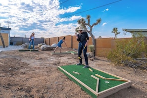 A backyard with a miniature golf course, a wooden fence, and a desert landscape.