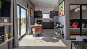 A modern kitchen with dark cabinets, a dining area with a round table and chairs, and a living area with a sofa and a TV. - Saltwater Pool/Sauna/Mini Golf/JT Nat Park/Firepit (Yucca Valley)