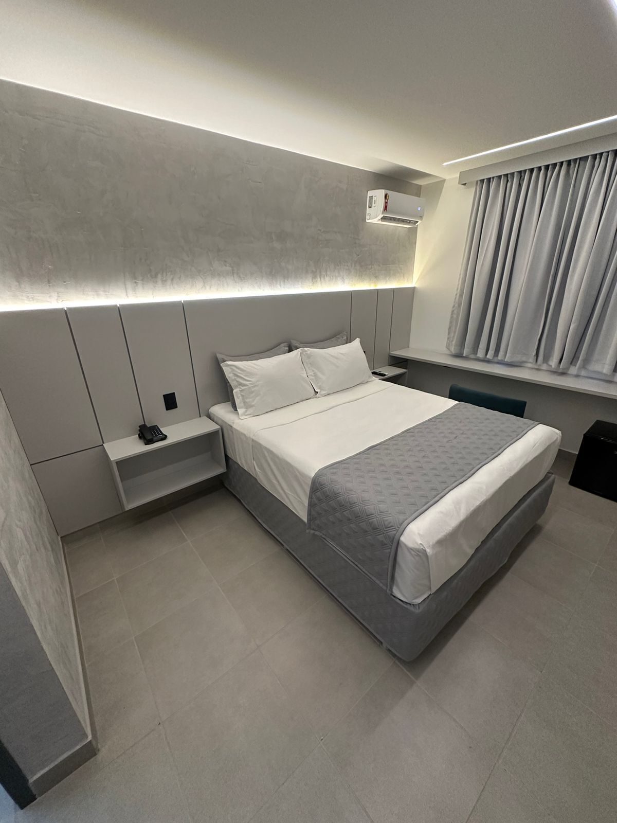 Een moderne hotelkamer met een groot bed, een nachtkastje met telefoon, en een raam met gordijnen.