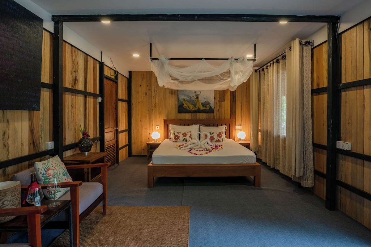 Un dormitorio con cama de madera, lámparas de noche, un banco y un cuadro en la pared.