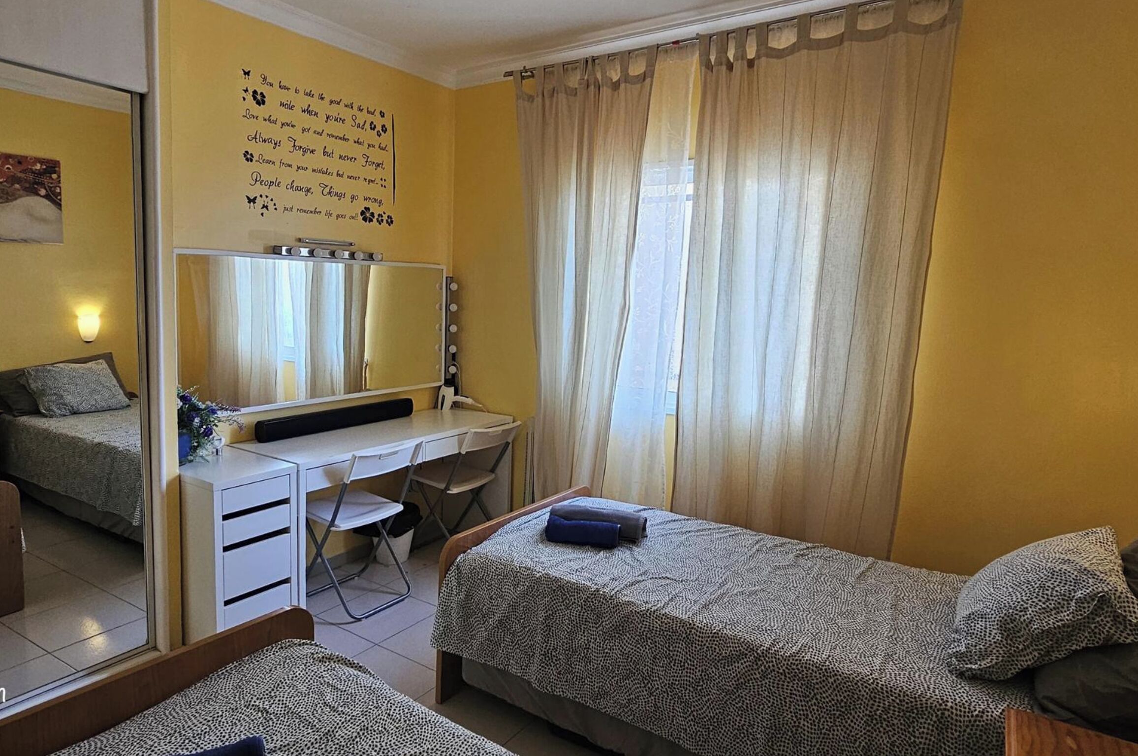 A room with a bed, a desk with a mirror, and a window with curtains.