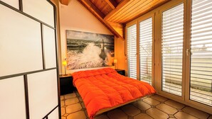 Ein Schlafzimmer mit Bett, einem Gemälde eines Leuchtturms und Blick durch das Fenster.