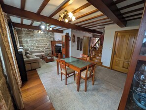 A cozy living room with a stone wall, wooden furniture, a dining table, and a staircase leading upstairs. - Villa sea Views With Park in Front of the Beach (Cangas)