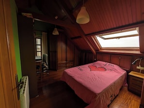 A bedroom with a wooden ceiling, a skylight, a bed with a pink bedspread, a desk with a chair, and a wardrobe. - Villa sea Views With Park in Front of the Beach (Cangas)