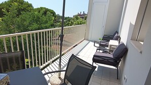 En balkong med ett bord och stolar, ett stort parasoll och utsikt över grönska och hus i bakgrunden.