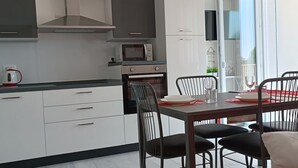 Ett modernt kök med vita skåp, en mikrovågsugn och en spis. Här finns ett matbord med fyra stolar och en röd accentfåtölj.
