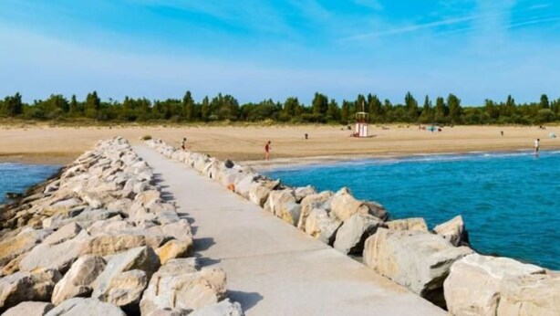 En strandpromenad längs kusten med en stenmur som leder ner till en sandstrand.