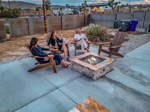 A group of people seated around a fire pit in an outdoor patio area. - Tiny Home w Pool, Hot Tub, Sauna, Golf & More! (Yucca Valley)