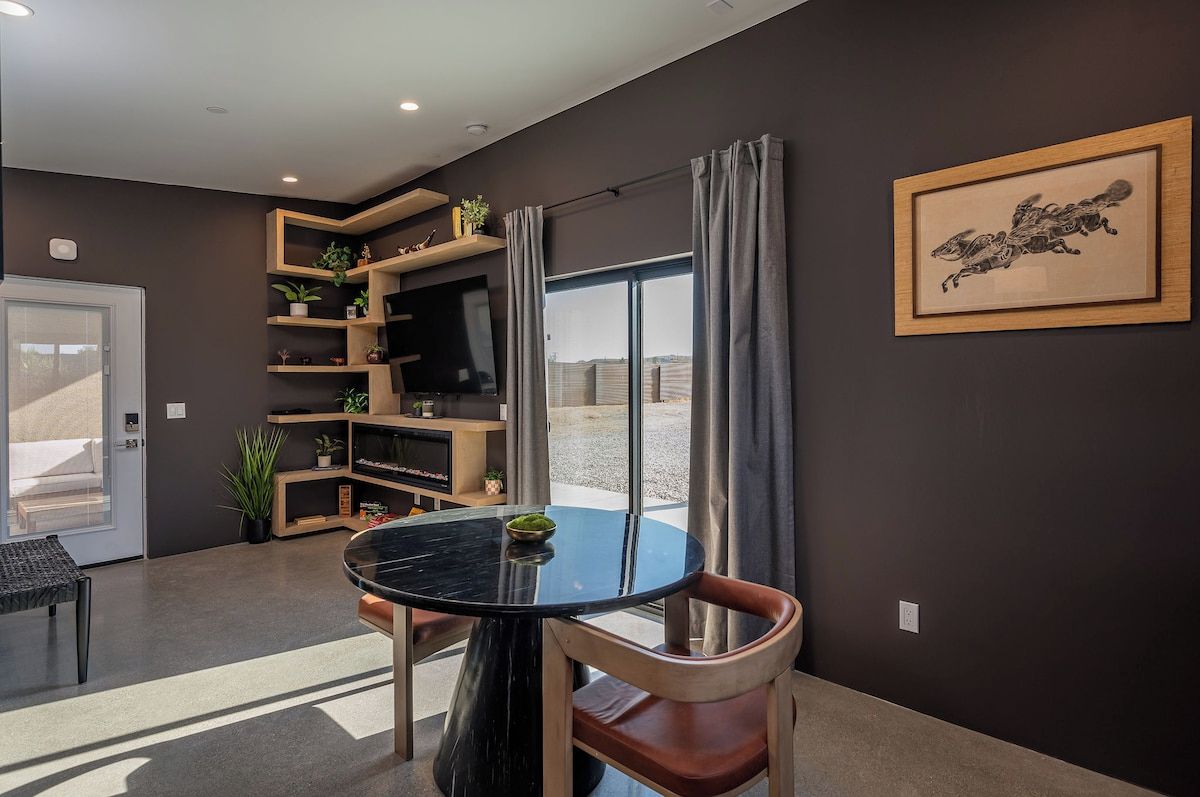 Een moderne woonkamer met een ronde zwarte tafel, een televisie op een houten dressoir en een lijstwerk op de muur.