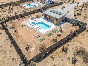 A modern house with a swimming pool, a fenced yard, and desert vegetation.