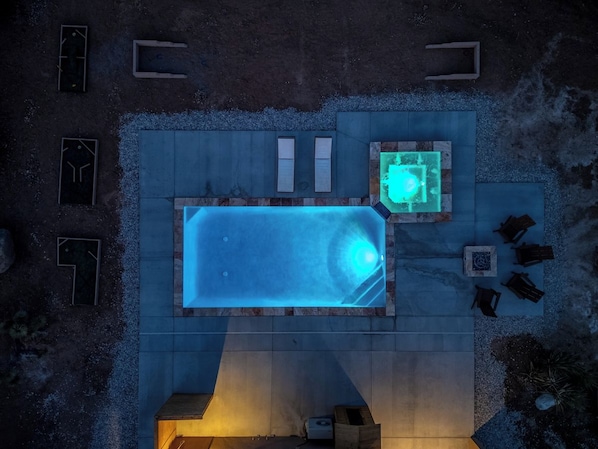 A rooftop swimming pool with a hot tub, surrounded by seating areas and a fire pit.
