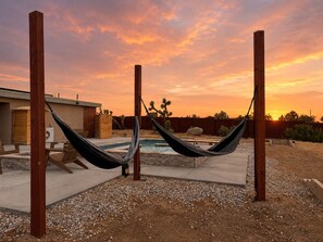 A hammock setup in a backyard with a pool and a house in the background.