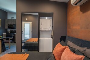 A compact room with a bed, a small kitchenette, and a built-in washer-dryer unit. - Tiny Home w Pool, Hot Tub, Sauna, Golf & More! (Yucca Valley)
