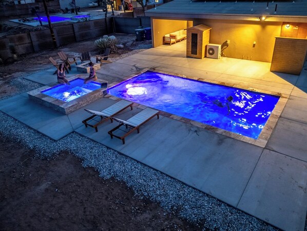 A swimming pool with a hot tub and lounge chairs, surrounded by a patio area.
