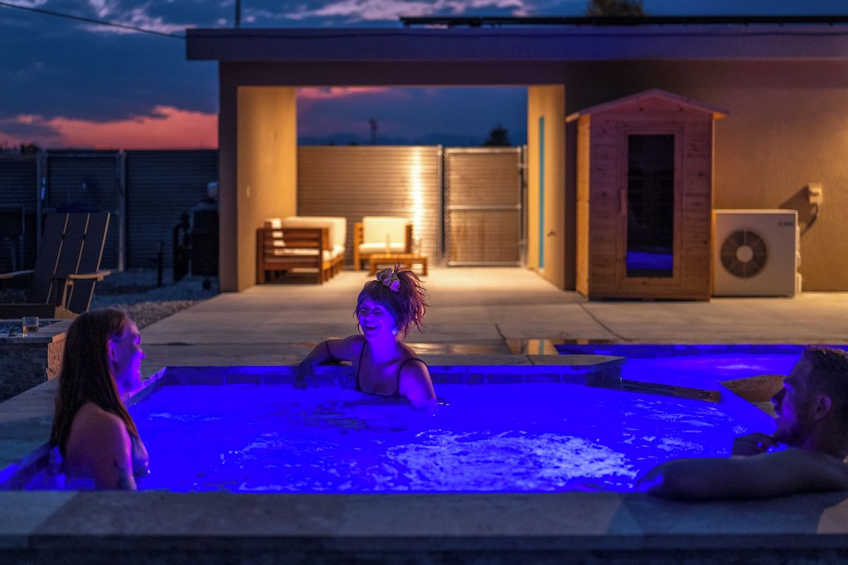 A swimming pool area with a covered deck, a sauna, and a small building structure.
