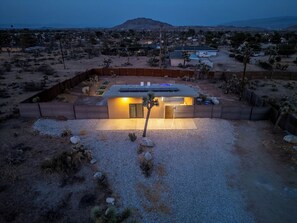 Aerial twilight view of the lit tiny home in its fenced desert lot