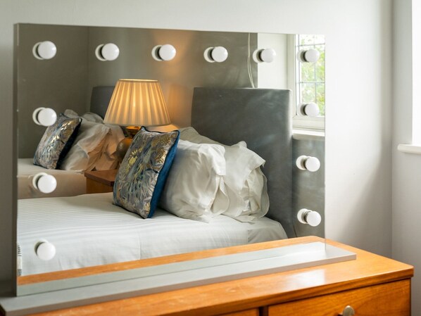 Une chambre avec un grand miroir, un lit avec de nombreux oreillers, une table de chevet et une lampe.