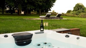 A hot tub with a built-in grill, a wine bottle, and two glasses of wine on a table.