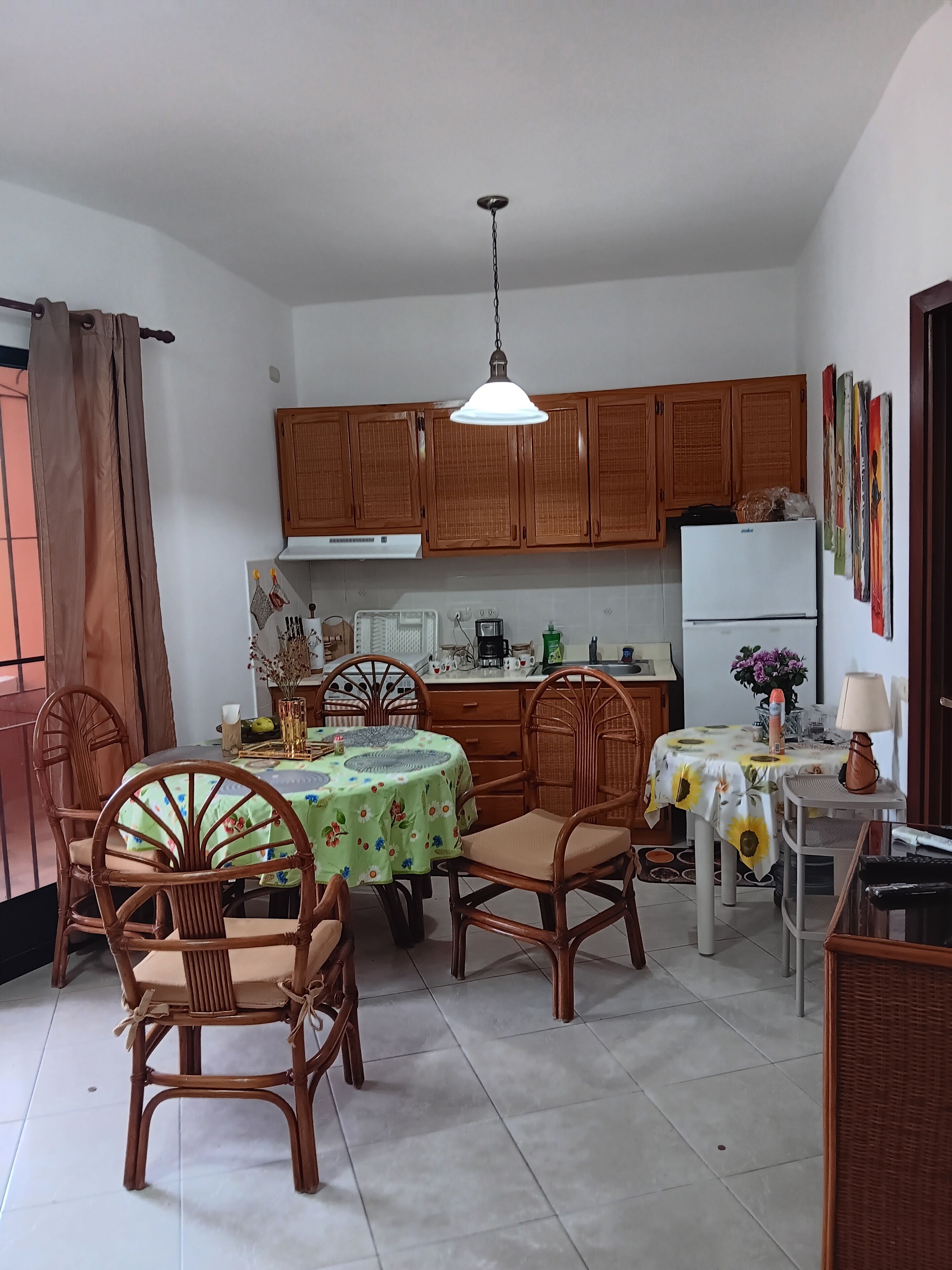 Cucina con mobili in legno, tavolo da pranzo con sedie, frigorifero e lampadario.