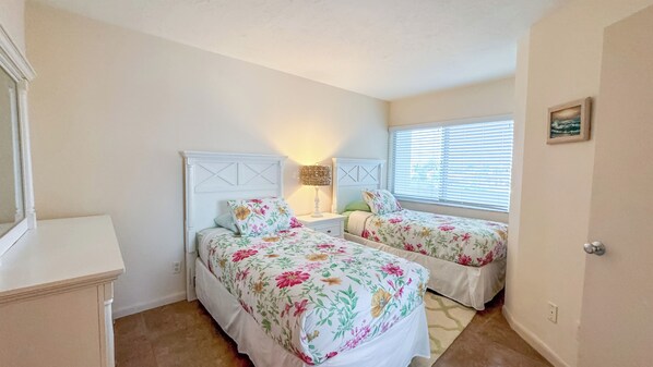 Un dormitorio con dos camas, una mesita de noche, una lámpara y una ventana con persianas.