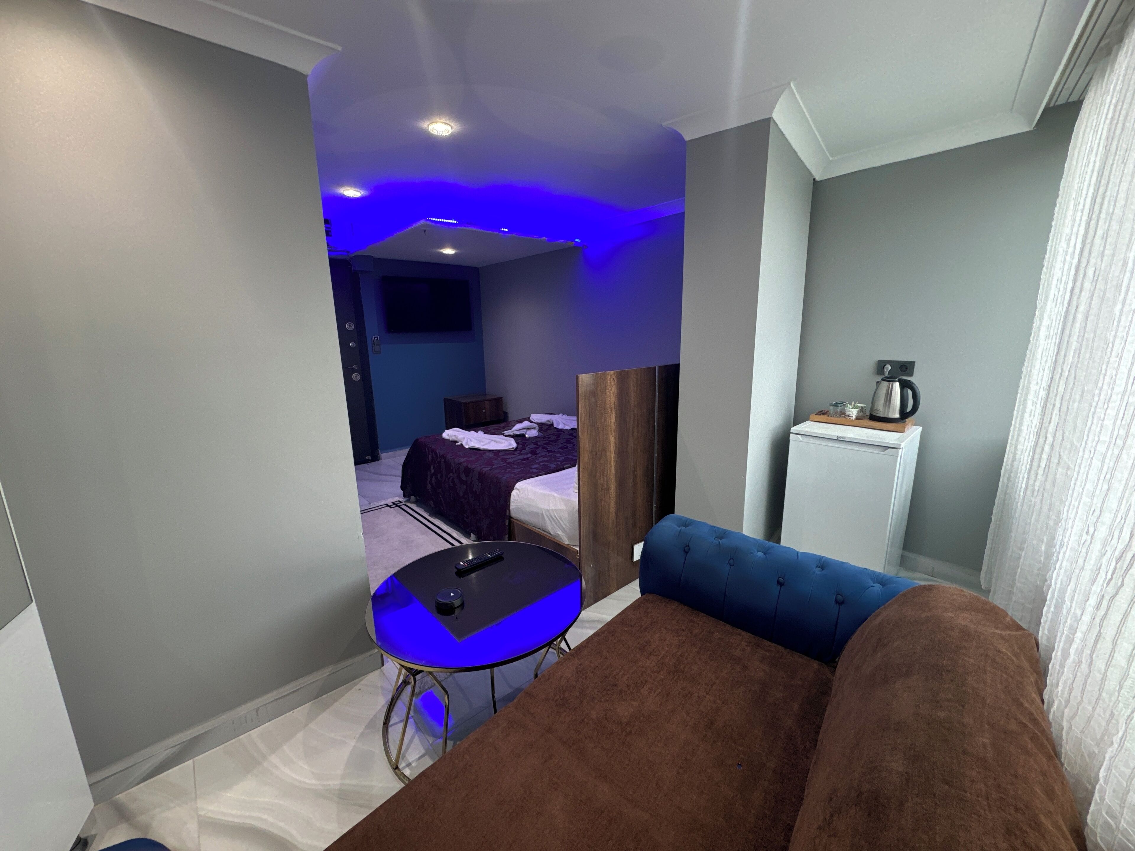 Una habitación de hotel con una cama, una mesita con un control remoto, un sofá azul y una zona de kitchenette.
