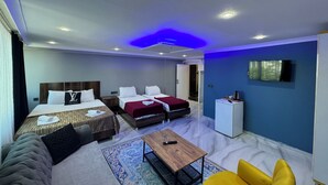 Una habitación de hotel moderna con dos camas, un sofá, una mesita, un televisor y un mini bar.