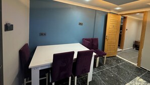 Un comedor con mesa blanca y sillas moradas, pared azul y puerta de madera.