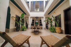Un ampio cortile con zona pranzo centrale, circondato da sedie in vimini e piante in vaso.