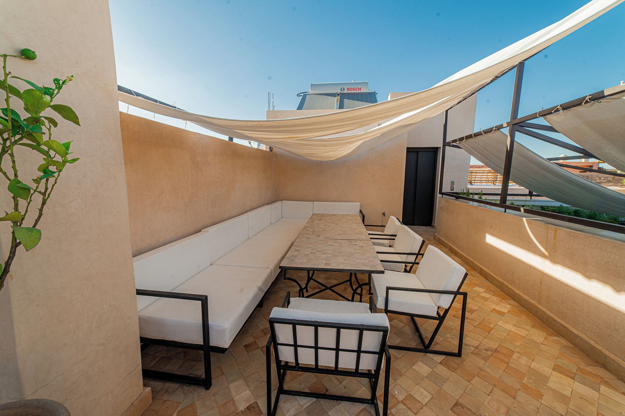A rooftop terrace with a long bench, a table, and chairs.