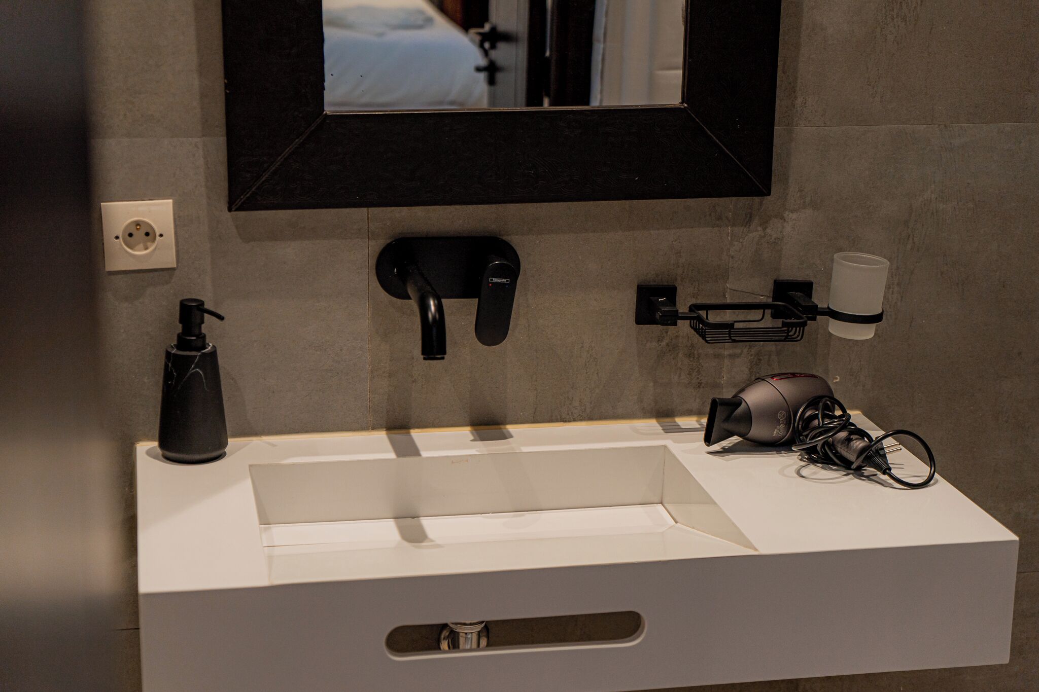 A modern bathroom with a white sink, a black faucet, a hairdryer, and a mirror above the sink.