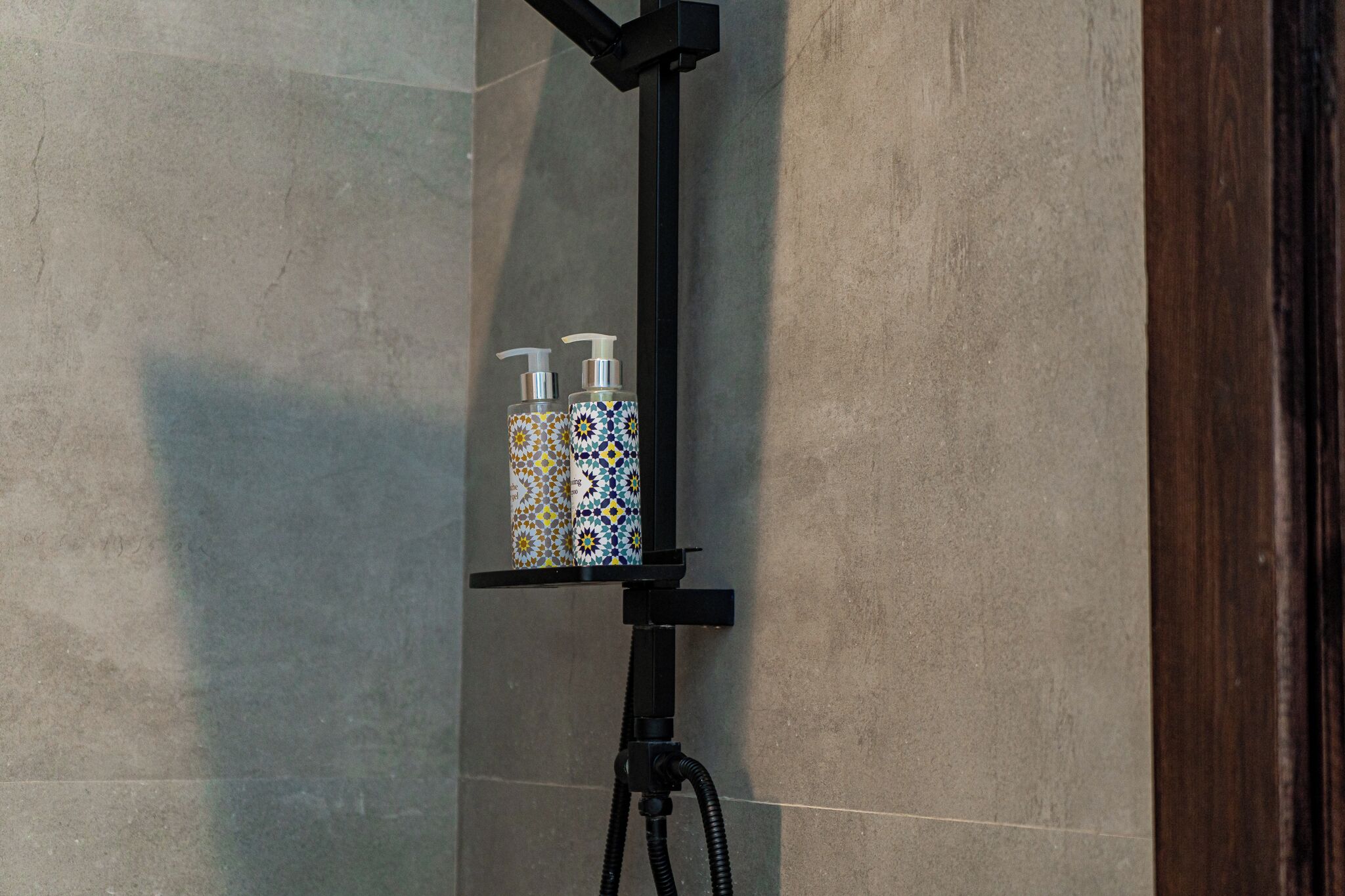 A shower area with a black towel rack holding two bottles of soap.