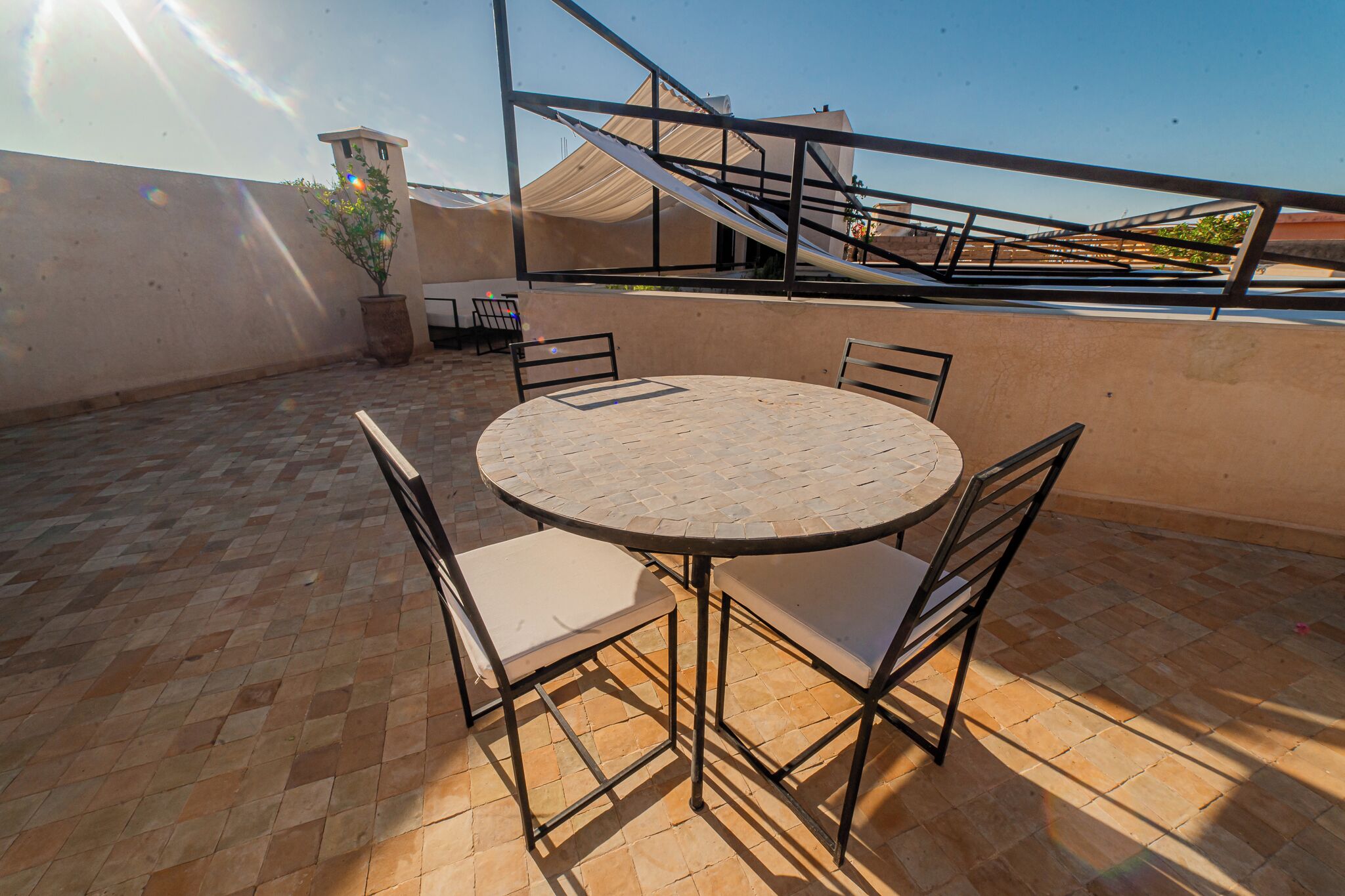 A round table with four chairs, a potted plant, and a staircase in the background.